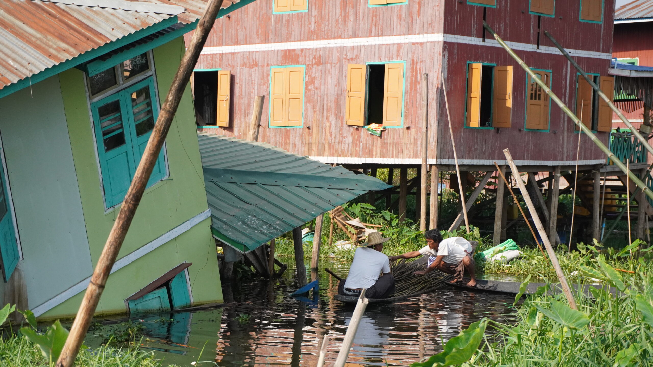 A photo showing broken houses in the middle of the lake, a man and a woman are in a small boat rowing towards the devastation.
